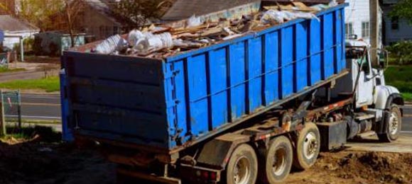 full blue dumpster being driven away on back of truck